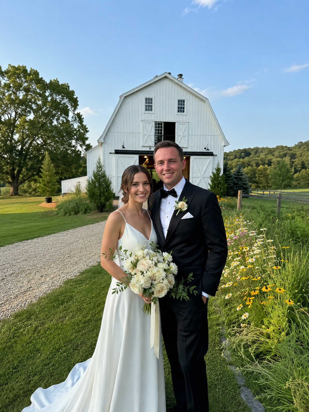 Bride and groom smiling in front of a white barn